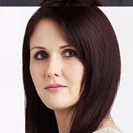 A woman with straight dark brown hair and light skin looks into the camera. She is wearing a white top, and the background is plain white.